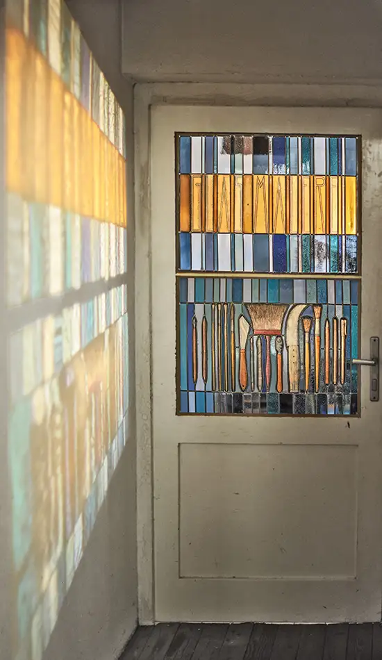 Stained glass window at Tiroler Glasmalerei with depictions of tools used in glass painting and Art Nouveau lettering