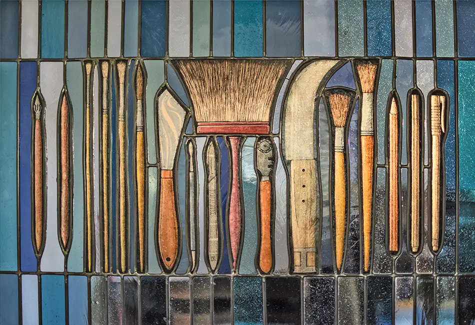 Stained glass window at Tiroler Glasmalerei with depictions of tools used in glass painting