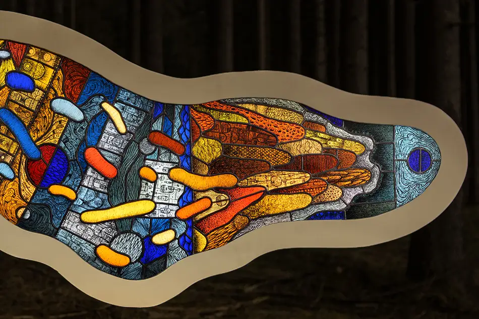 Detail of a free-hanging and illuminated stained glass window with detailed painting which is named Amoeba and hangs in a forest