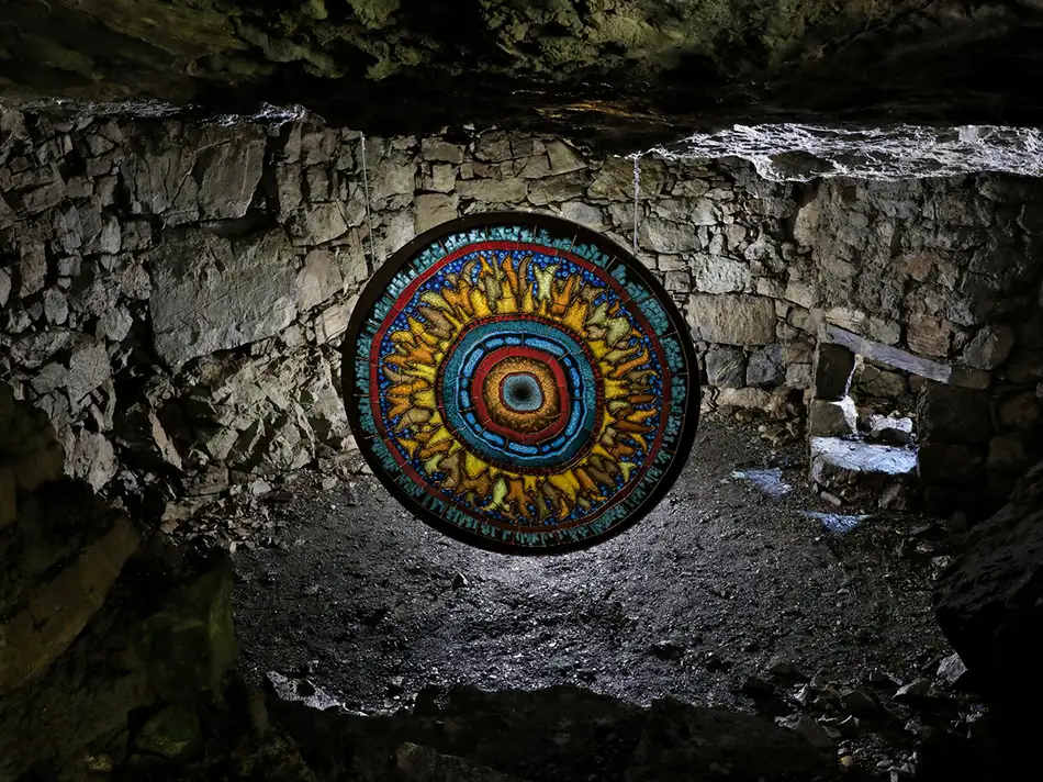 Detailed painted stained glass reminiscent of a gigantic fluorescent cell hanging as an art object in a cave.