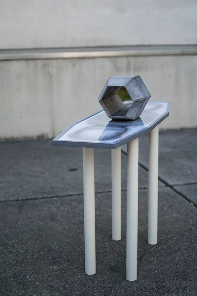 Artwork made of concrete, mirror and digital print which is reminiscent of a table on which a geometric concrete element stands in the centre of which a mirror is fixed.