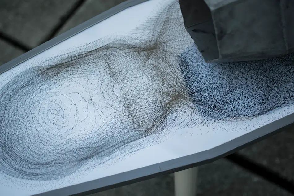 Detail of an artwork made of concrete, mirror and digital print which is reminiscent of a table on which a geometric concrete element stands in the centre of which a mirror is fixed.
