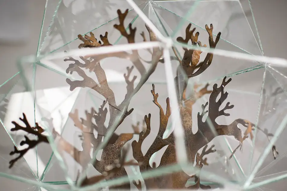 Artwork reminiscent of a greenhouse, consisting of a geometric glass enclosure, a concrete plinth and a plant-like steel structure - detail