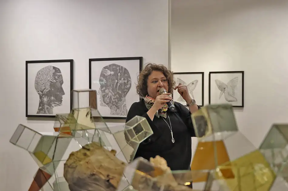 Crystalis V - geometric glass artwork on a piece of driftwood - exhibition view - Curator Karin Pernegger during the opening speech of Below the Surface Is Another Surface at Galerie Platform 6020, Innsbruck.
